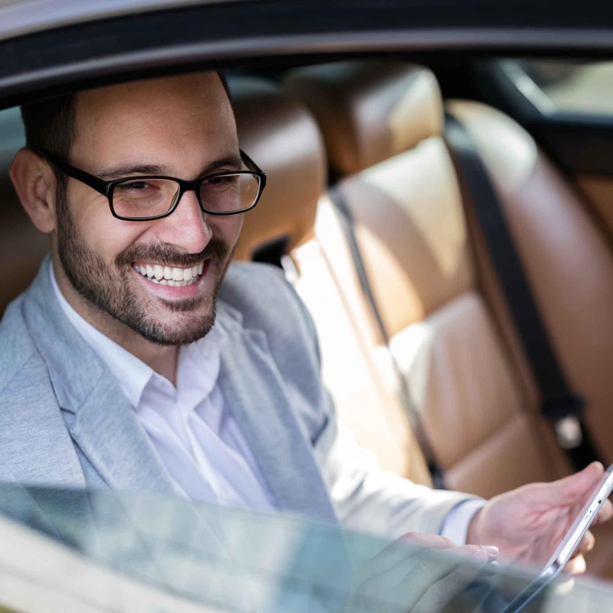 A smiling business professional reading a tablet in a car